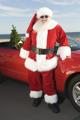 Father Christmas stands by red convertible with Christmas tree