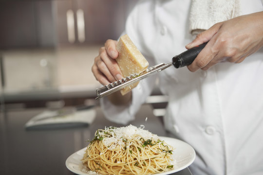 Midsection of female chef grating cheese onto pasta in kitchen