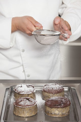 Midsection closeup of male chef icing sugar over chocolate cakes at counter in commercial kitchen