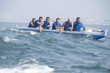 Male rowers paddling outrigger canoe in race