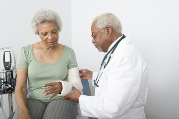 An African American male doctor checking patient's fractured hand at clinic