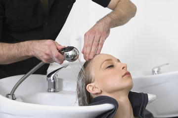 Closeup of young woman getting hair wash from hairdresser in salon