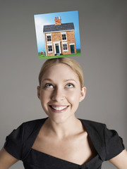 Model home on top of young woman's head representing homeownership