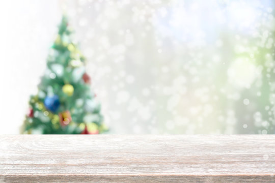 Wood table top on blur with bokeh christmas tree background with snowfall - can be used for display or montage your products