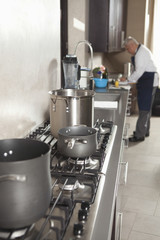Closeup of utensils on stove with chef working in background at commercial kitchen