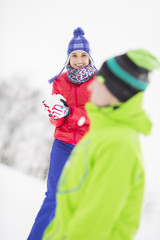 Fototapeta na wymiar Smiling young woman having snowball fight with male friend
