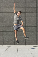 Full length of excited jogger jumping against tiled wall