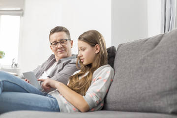 Father and daughter using digital tablet on sofa at home