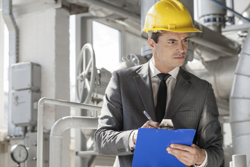 Young male supervisor writing on clipboard in industry