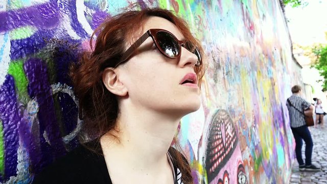 closeup footage of a woman leaning against a wall full of murals