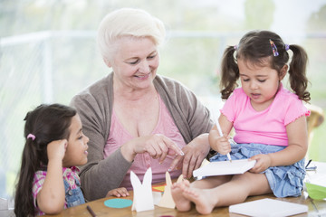 Happy senior woman assisting granddaughters in making handicraft at home