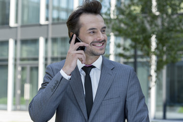 Happy businessman conversing on cell phone outside office