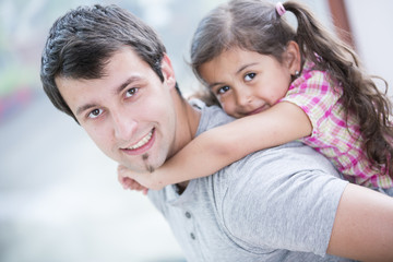 Side view portrait of smiling man piggybacking little daughter at home