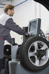 Obraz na płótnie Canvas Side view of mid adult male mechanic repairing car's wheel in workshop