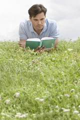 Naklejka na ściany i meble Man reading book while lying on grass against sky