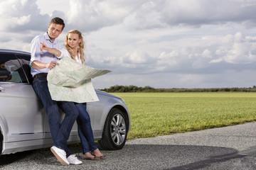 Fototapeta premium Full length of couple with map discussing direction while leaning on car at countryside