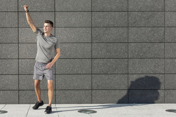 Full length of young jogger with clenched fist standing against tiled wall