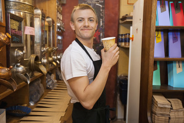 Portrait of male salesperson holding disposable coffee cup in store