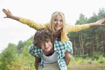 Portrait of happy woman enjoying piggyback ride on man in forest