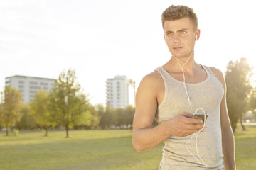 Young jogger looking away while listening music through cell phone in park