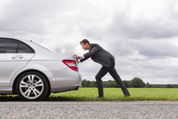 Full length side view of young businessman pushing broken down car on road