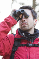 Young male backpacker using binoculars in forest