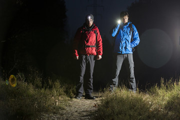 Full length portrait of male hikers with flashlights in field at night - obrazy, fototapety, plakaty