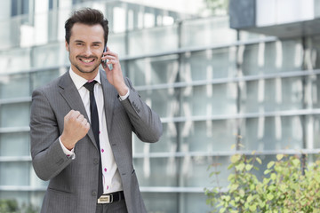 Portrait of successful young businessman using cell phone against office building