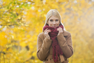 Portrait of beautiful woman holding muffler around neck in park during autumn
