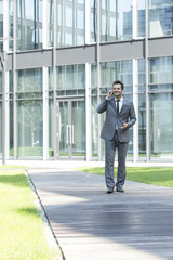 Smiling businessman using mobile phone while walking on path outside office