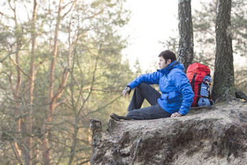 Side view of hiker sitting on edge of cliff in forest