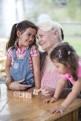 Loving grandmother teaching calculation to granddaughters at table in house