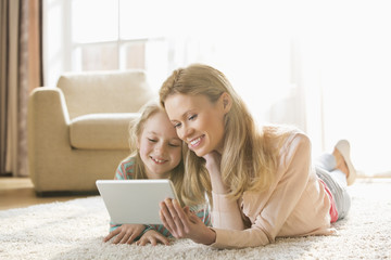 Mother and daughter using digital tablet on floor at home