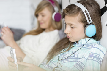 Sisters listening music through headphones at home