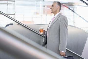 Side view of middle aged businessman with coffee cup walking up stairs in railroad station