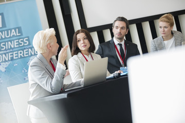 Business people talking while sitting at desk in seminar hall