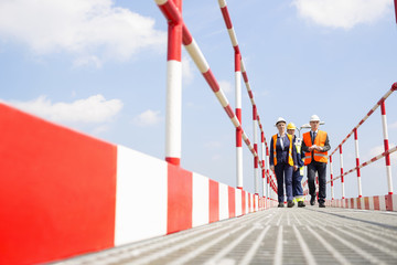 Full-length of workers walking on footbridge against sky