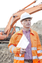 Architect looking away while holding clipboard at construction site