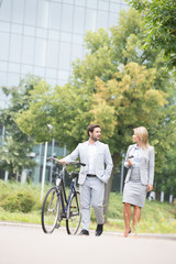 Businesspeople with bicycle conversing while walking on street