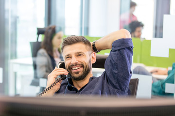 Smiling mid adult businessman talking on phone in office - obrazy, fototapety, plakaty