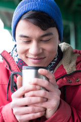 Smiling man looking at coffee in insulated drink container during winter