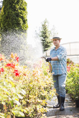 Full-length of man watering plants outside greenhouse