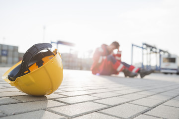 Yellow hardhat at shipyard with depressed male worker in background