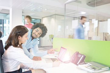 Fototapeta premium Young businessman and businesswoman discussing over laptop in office