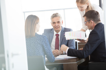 Portrait of confident mature businessman with colleagues in meeting room