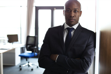 Portrait of young businessman standing arms crossed leaning on cupboard in office