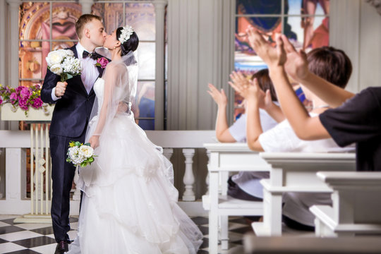 Wedding guests applauding while newlywed couple kissing in church