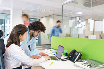 Young businessman and businesswoman using laptop at desk in office