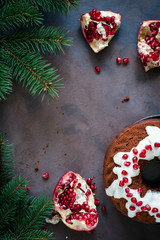 Chocolate bundt cake with cream cheese glaze and pomegranate seeds, fresh pomegranate and fir tree branches creating frame. Copy space for text.