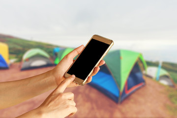 woman hand holding and touch screen of smartphone,tablet,cell phone over Colorful of Camping Tent with Fog on Hill